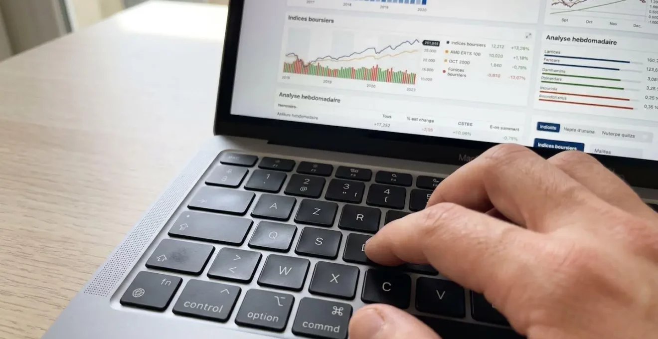 Gros plan d'une main tapant sur un clavier d'ordinateur portable avec écran flouté montrant des graphiques en arrière-plan